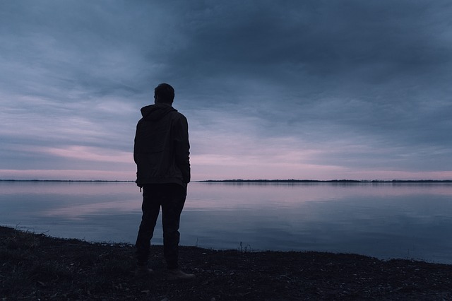 Muž v bunde stojí pri jazere počas súmraku